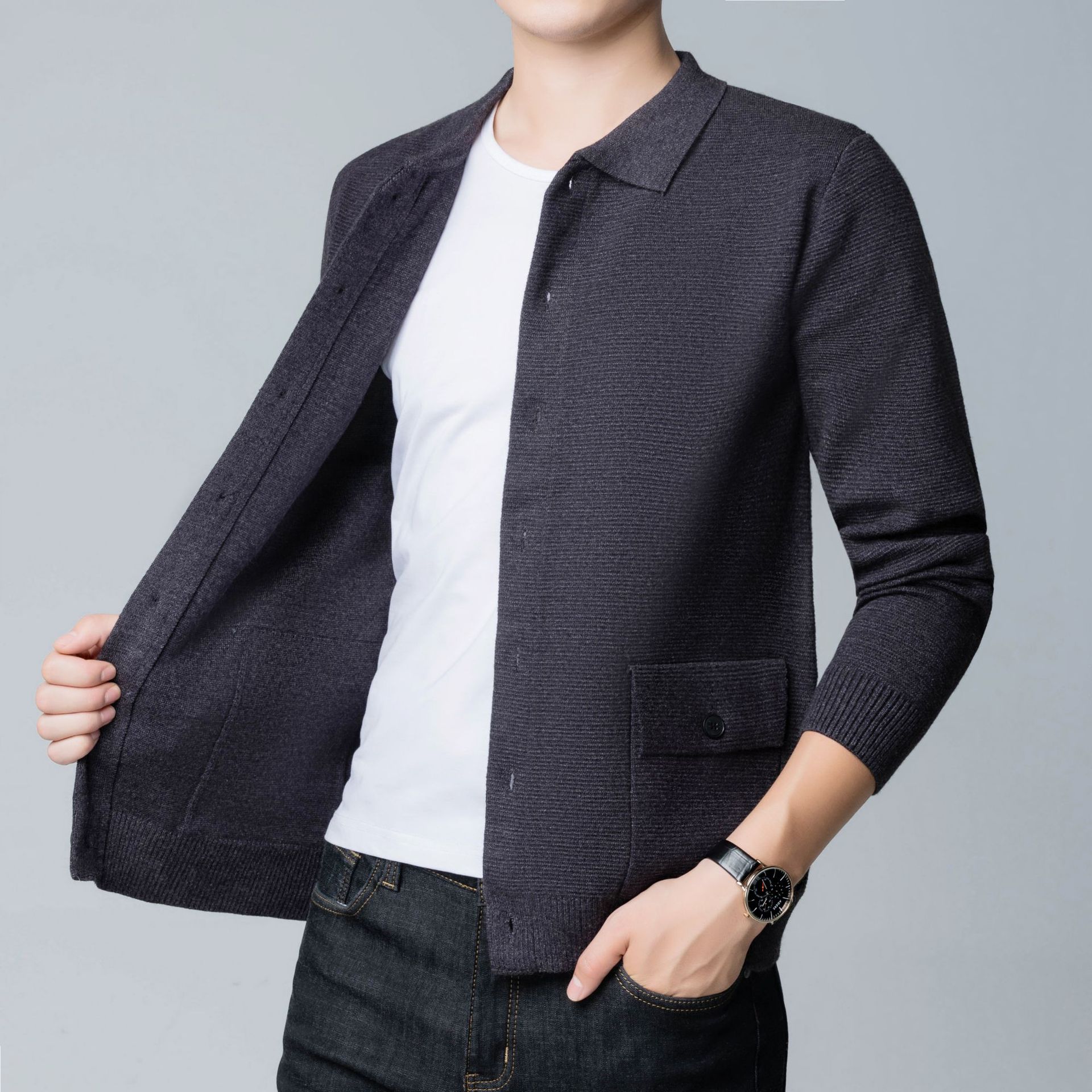 Uomo in camicia bianca e cardigan grigio scuro, orologio elegante al polso, moda casual maschile, abbigliamento autunnale, sfondo grigio chiaro.