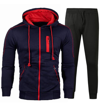 Tuta sportiva uomo blu e rossa con cappuccio e pantaloni neri, design moderno, ideale per fitness e tempo libero.