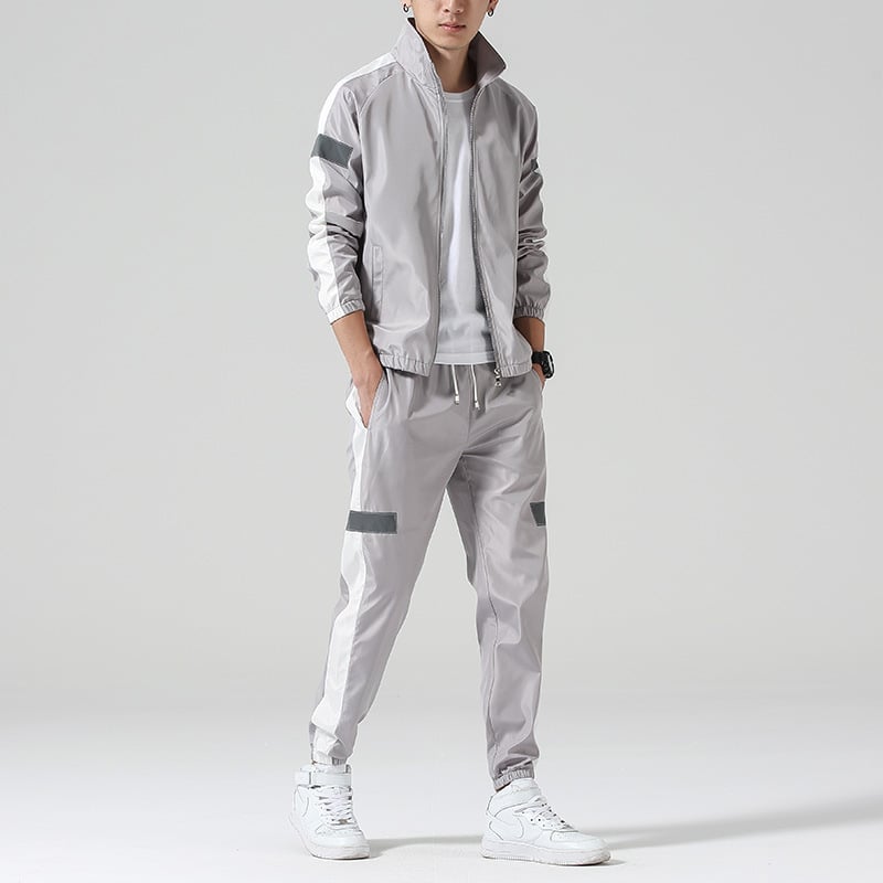 Giacca e pantaloni sportivi grigi da uomo, con dettagli a righe nere, abbinati a scarpe da ginnastica bianche. Look casual e moderno.