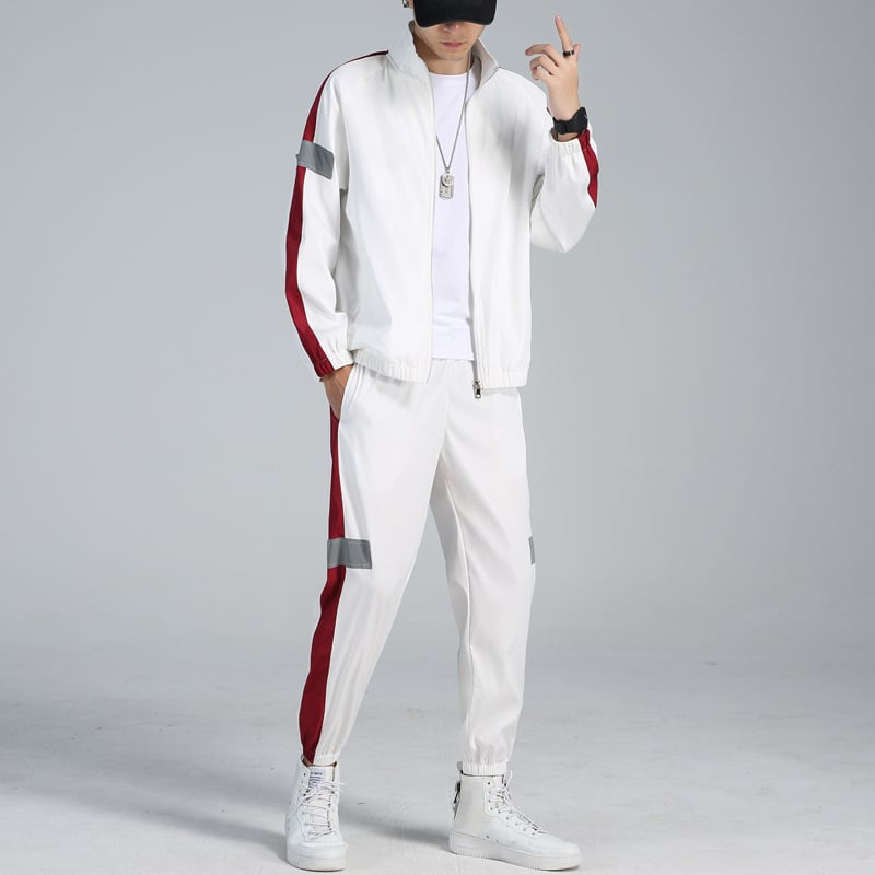 Uomo in tuta sportiva bianca con strisce rosse, cappellino nero e scarpe da ginnastica bianche. Moda casual, abbigliamento sportivo uomo.
