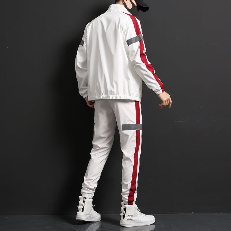 Uomo in tuta sportiva bianca con strisce rosse e grigie, scarpe da ginnastica bianche, sfondo nero. Moda streetwear, abbigliamento casual.