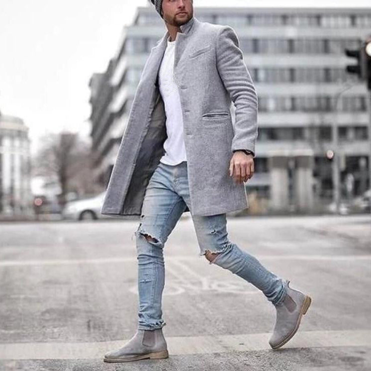 Uomo con cappotto grigio elegante, jeans strappati e stivali alla moda cammina in città. Look urbano, stile invernale, moda maschile contemporanea.