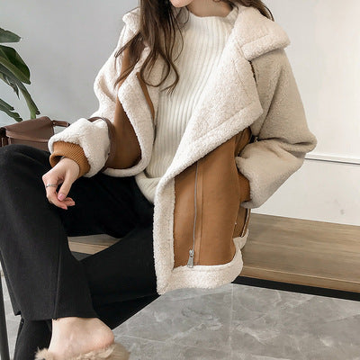Donna seduta indossa giacca invernale in shearling beige e marrone, maglione bianco, pantaloni neri. Moda autunnale, abbigliamento casual elegante.