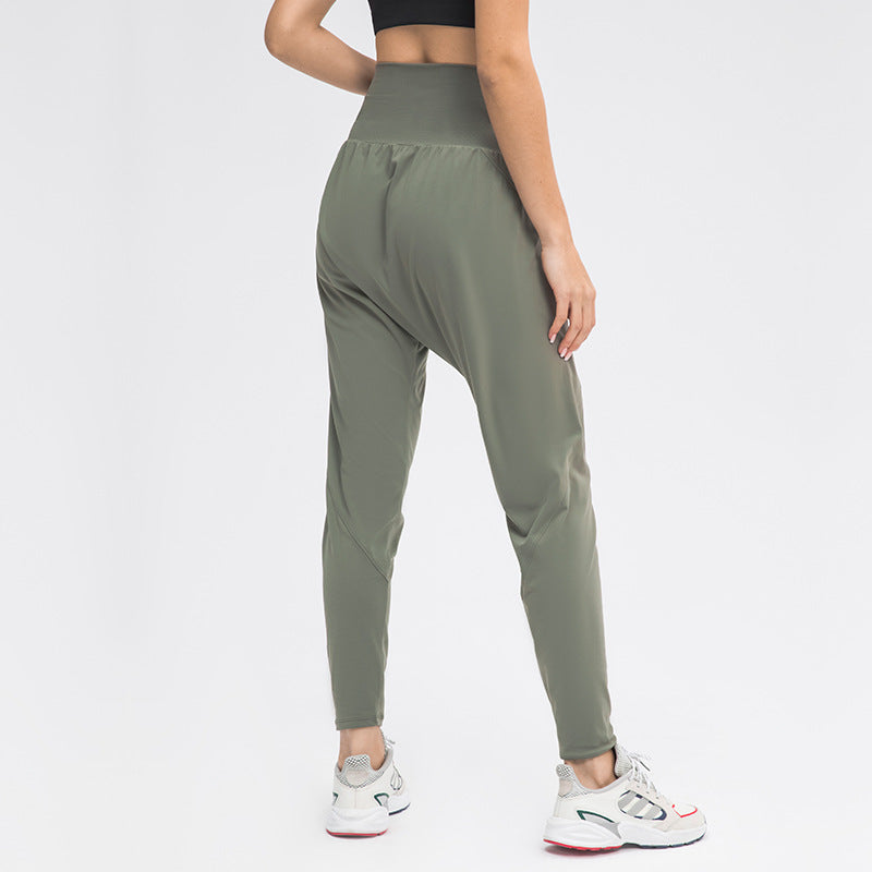 Pantaloni sportivi donna verde oliva, vita alta, tessuto elastico, abbinati a scarpe da ginnastica bianche. Abbigliamento fitness moderno.