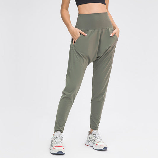 Donna in pantaloni sportivi verdi, vita alta, con tasche, abbinati a scarpe da ginnastica bianche e top nero. Abbigliamento fitness moderno.