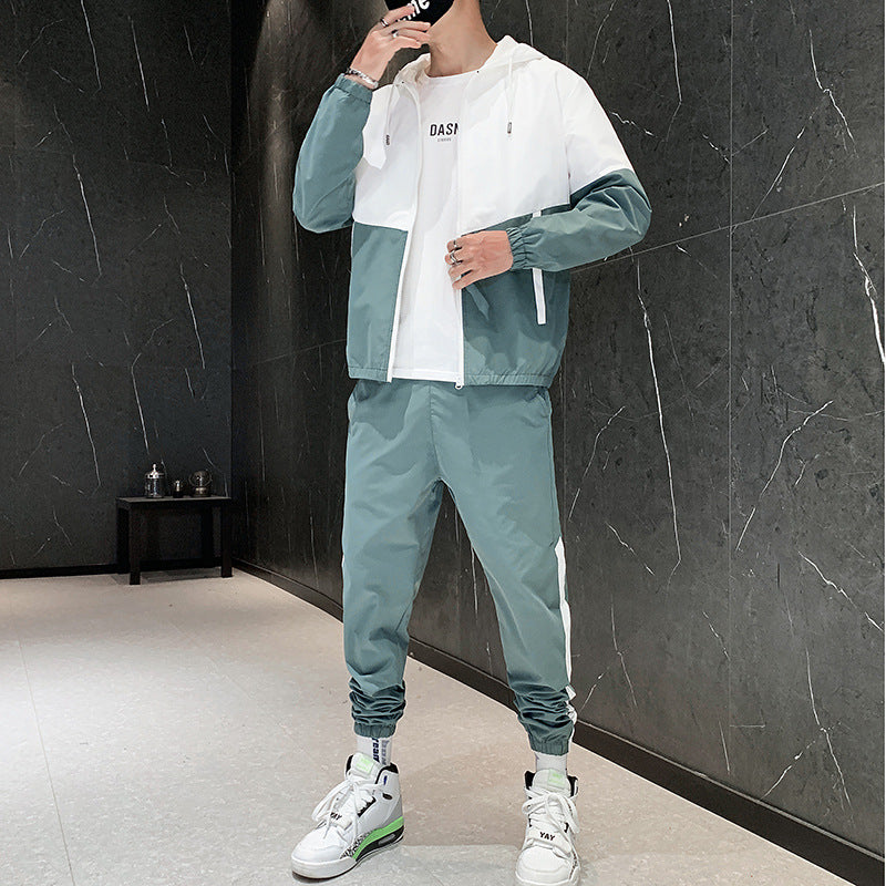 Uomo in tuta sportiva verde e bianca, scarpe da ginnastica bianche, posa in una stanza moderna con pareti scure. Moda casual, abbigliamento sportivo.