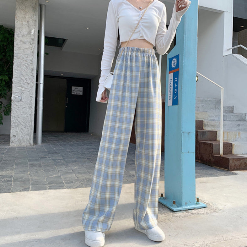 Donna con pantaloni a quadri blu e bianchi, top bianco a maniche lunghe, scarpe da ginnastica bianche. Moda casual, stile urbano.