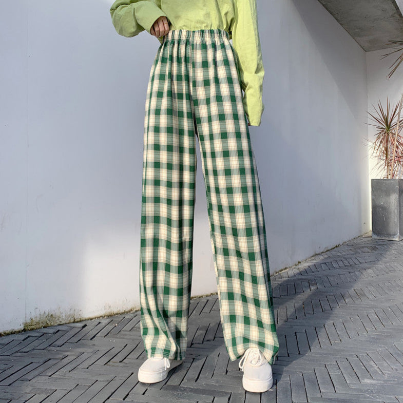 Pantaloni a quadri verdi e bianchi, stile casual, indossati con maglia verde chiaro e scarpe bianche, su sfondo urbano minimalista.