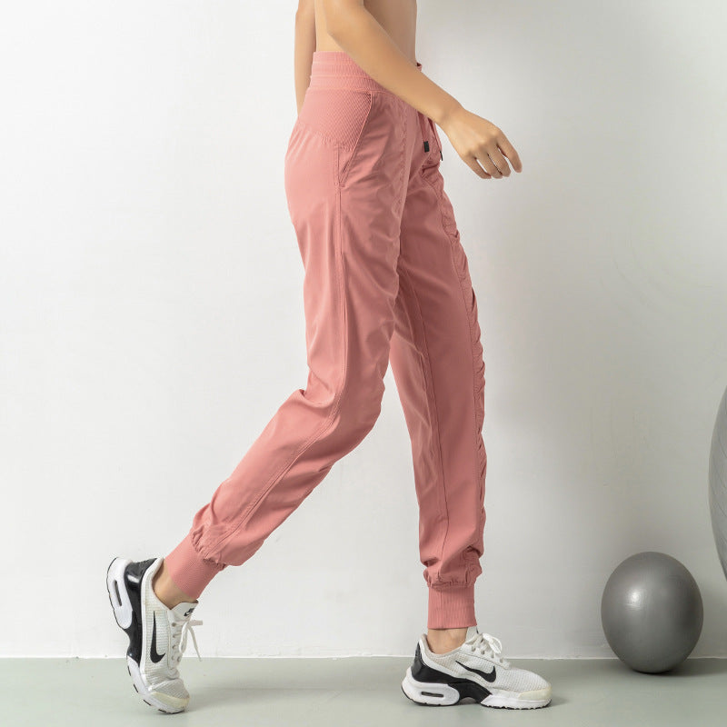 Pantaloni sportivi rosa da donna, design moderno, tessuto leggero, abbinati a scarpe da ginnastica bianche e nere, ideali per fitness e yoga.