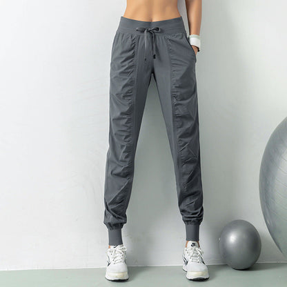 Pantaloni sportivi grigi da donna, design moderno, tessuto leggero, ideali per fitness e yoga. Scarpe da ginnastica bianche, palla da ginnastica grigia.