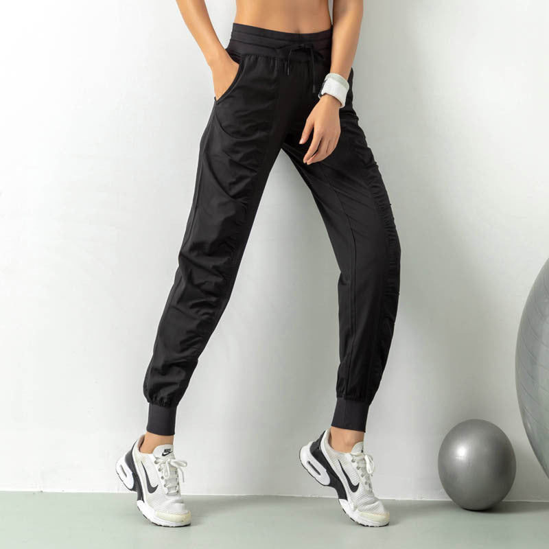 Donna in pantaloni sportivi neri, scarpe da ginnastica bianche, accanto a una palla da fitness grigia. Abbigliamento sportivo moderno e casual.