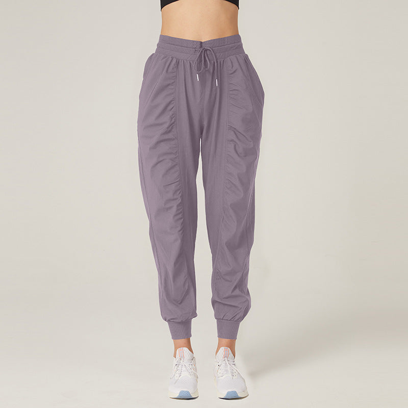 Pantaloni sportivi donna grigi, stile jogger, con tasche e coulisse, indossati con scarpe da ginnastica bianche. Abbigliamento casual e comodo.