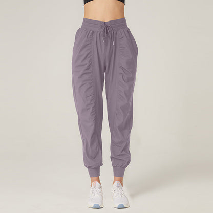 Pantaloni sportivi donna grigi, stile jogger, con tasche e coulisse, indossati con scarpe da ginnastica bianche. Abbigliamento casual e comodo.