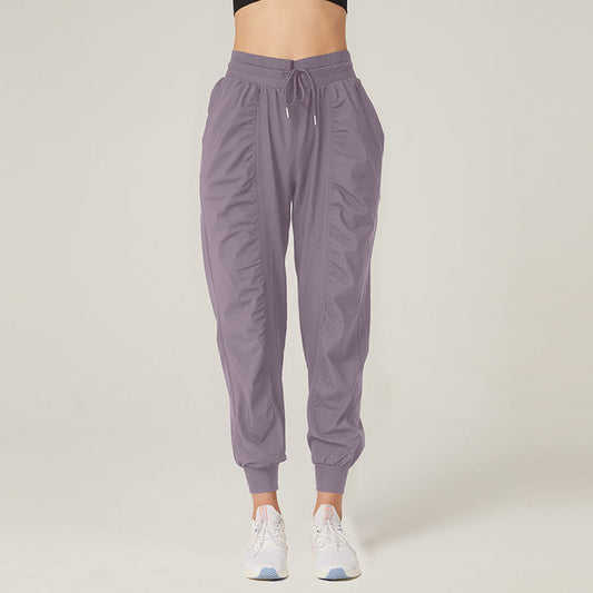 Pantaloni sportivi donna grigi, stile jogger, con tasche e coulisse, indossati con scarpe da ginnastica bianche. Abbigliamento casual e comodo.