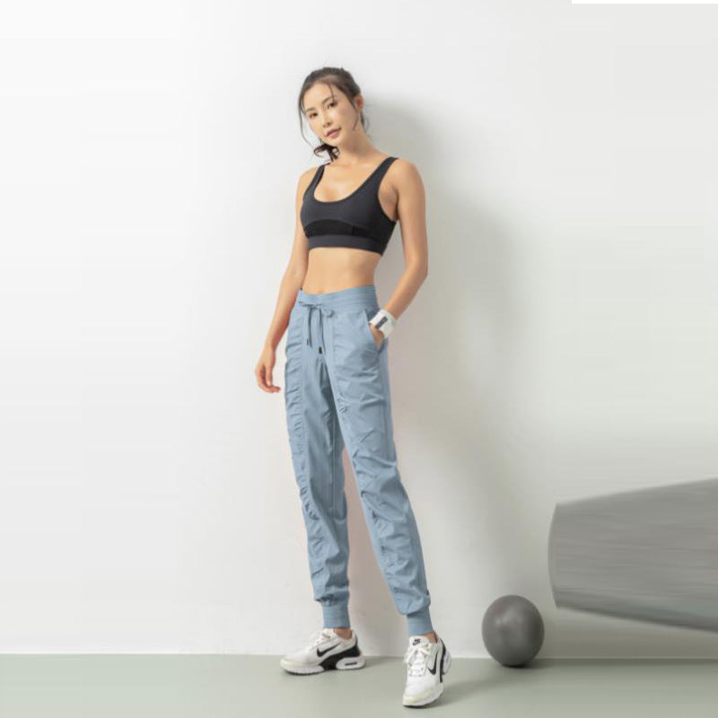 Donna in abbigliamento sportivo, top nero e pantaloni azzurri, posa accanto a una parete bianca con palla da fitness grigia. Fitness, moda sportiva.