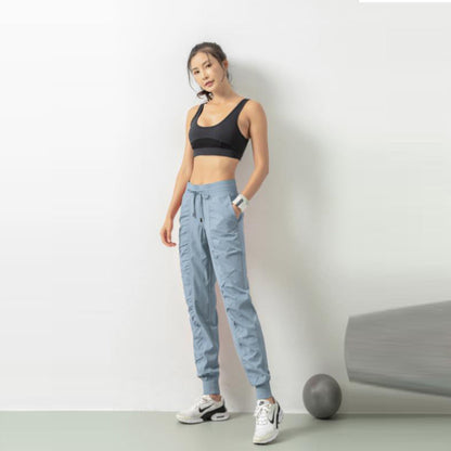 Donna in abbigliamento sportivo, top nero e pantaloni azzurri, posa accanto a una parete bianca con palla da fitness grigia. Fitness, moda sportiva.