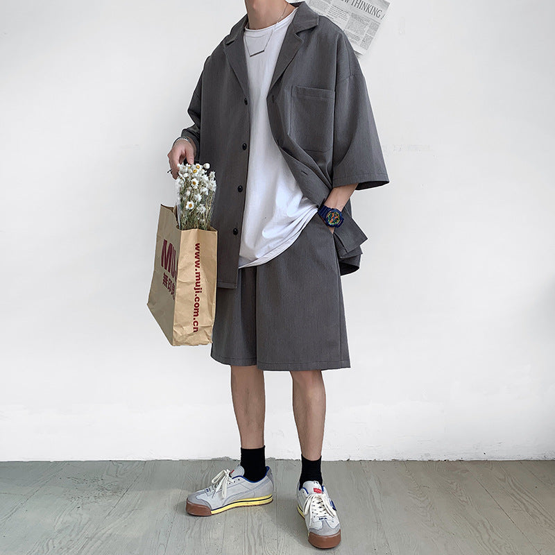 Uomo in abbigliamento casual estivo: camicia e pantaloncini grigi, t-shirt bianca, scarpe da ginnastica, borsa di carta, orologio colorato.