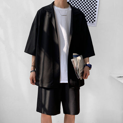 Uomo in abbigliamento casual estivo: camicia nera oversize, t-shirt bianca, pantaloncini neri, orologio blu, tiene un giornale. Moda maschile moderna.