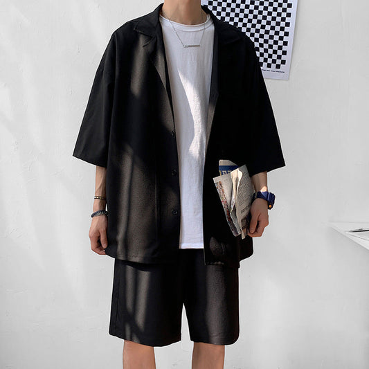 Uomo in abbigliamento casual estivo: camicia nera oversize, t-shirt bianca, pantaloncini neri, orologio blu, tiene un giornale. Moda maschile moderna.