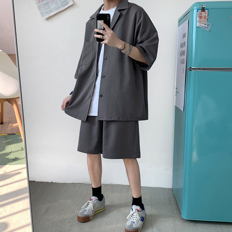 Uomo in abbigliamento casual estivo, indossa camicia e pantaloncini grigi oversize, scarpe da ginnastica colorate, accanto a frigorifero turchese.