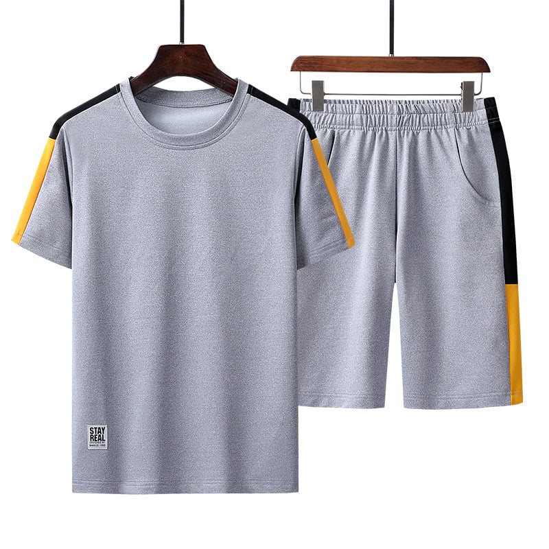 Completo sportivo estivo grigio per uomo, maglietta e pantaloncini con dettagli neri e gialli, tessuto traspirante, ideale per allenamento e tempo libero.