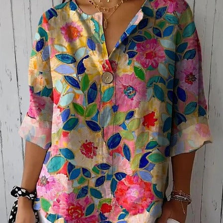 Camicia floreale colorata da donna con motivi di fiori e foglie su sfondo bianco, maniche a tre quarti, indossata con collane e bracciali.