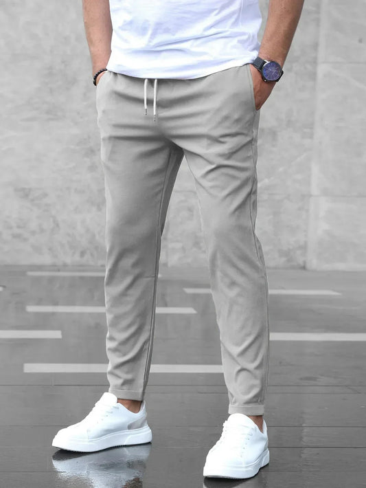 Uomo con pantaloni jogger grigi, t-shirt bianca e scarpe da ginnastica bianche su sfondo urbano. Moda casual maschile, stile moderno.