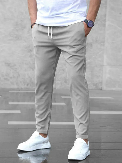 Uomo con pantaloni jogger grigi, t-shirt bianca e scarpe da ginnastica bianche su sfondo grigio. Moda casual maschile, abbigliamento sportivo elegante.