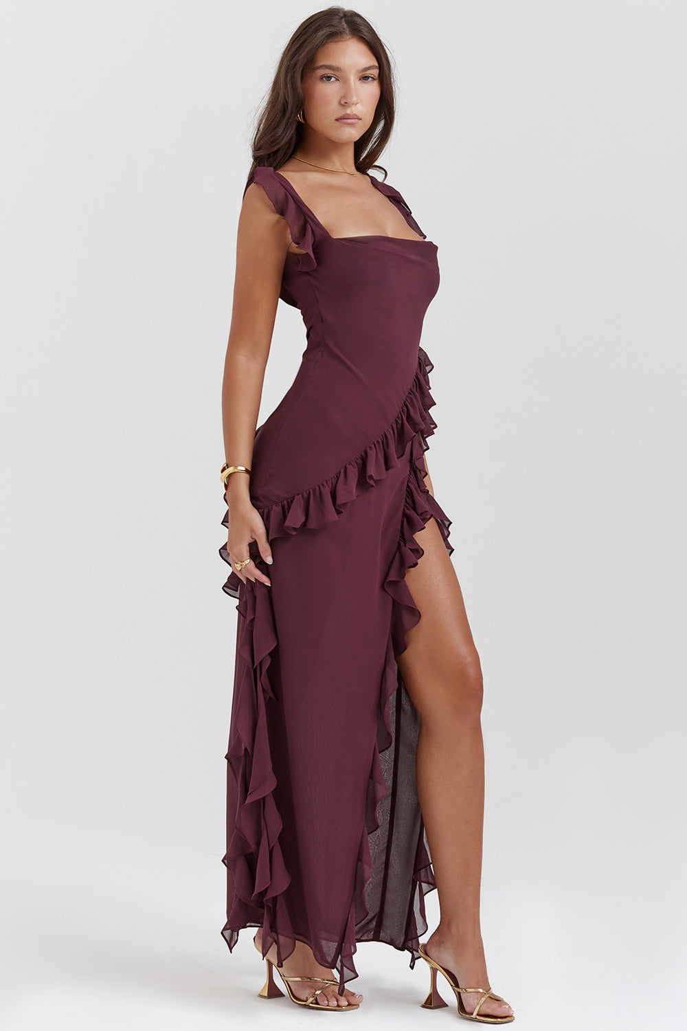Donna in abito lungo bordeaux con volant, spacco laterale e sandali dorati. Moda elegante, abbigliamento da sera, tendenze 2023.