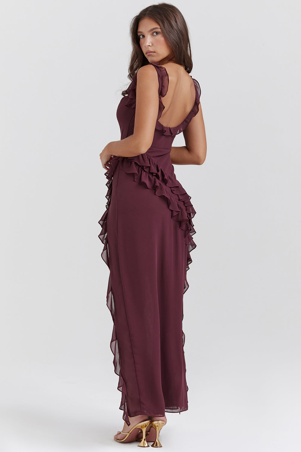 Donna in abito lungo bordeaux con volant, sandali dorati. Moda elegante, abbigliamento da sera, tendenza abiti femminili.
