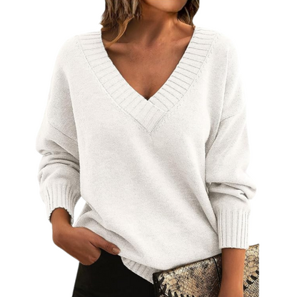 Donna con maglione bianco a V, maniche lunghe, tiene una pochette con stampa serpente. Moda autunnale, abbigliamento casual elegante.