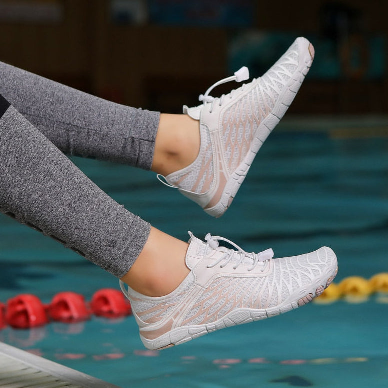 Scarpe da ginnastica bianche leggere e traspiranti indossate da una persona vicino a una piscina. Design moderno, ideali per sport acquatici.