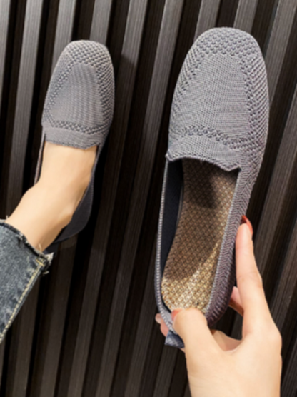Scarpe mocassini grigie in maglia, design casual ed elegante, su sfondo a righe. Scarpe comode per donna, ideali per look quotidiani.