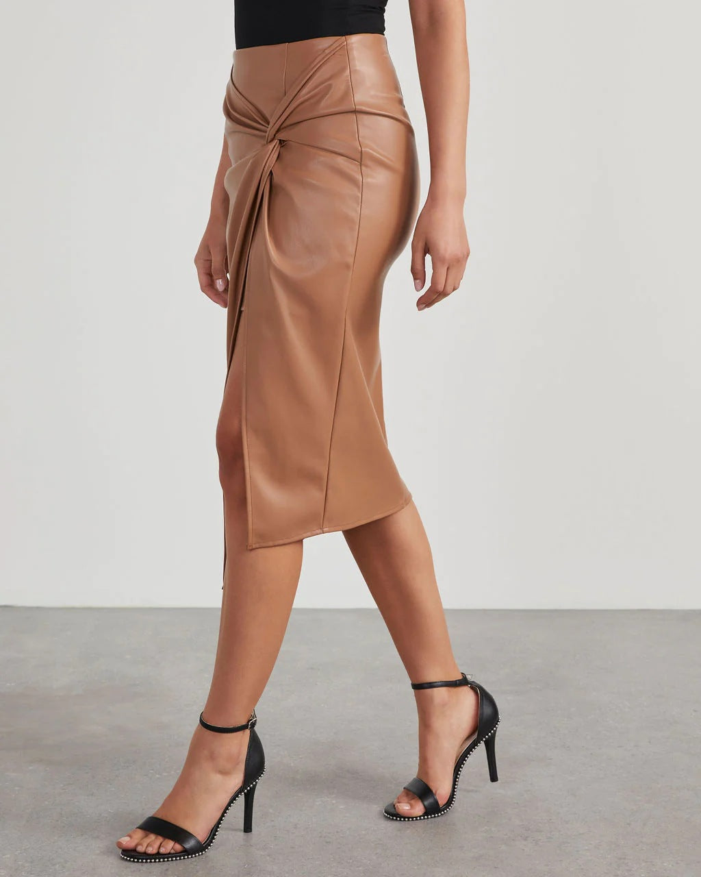 Gonna midi in ecopelle marrone con nodo frontale, indossata con sandali neri con tacco. Look elegante e moderno per moda donna autunno.