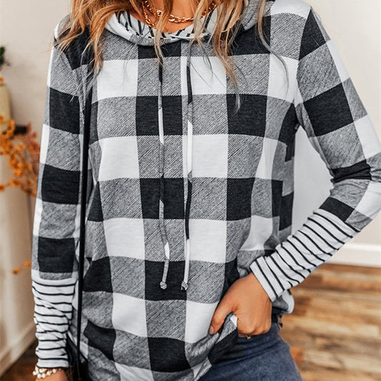 Donna con felpa a quadri bianco e nero, maniche a righe, in ambiente interno. Moda casual autunno, abbigliamento femminile trendy.