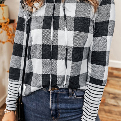 Donna con maglia a quadri bianco e nero, jeans blu, in un ambiente interno. Moda autunno, abbigliamento casual, stile moderno.