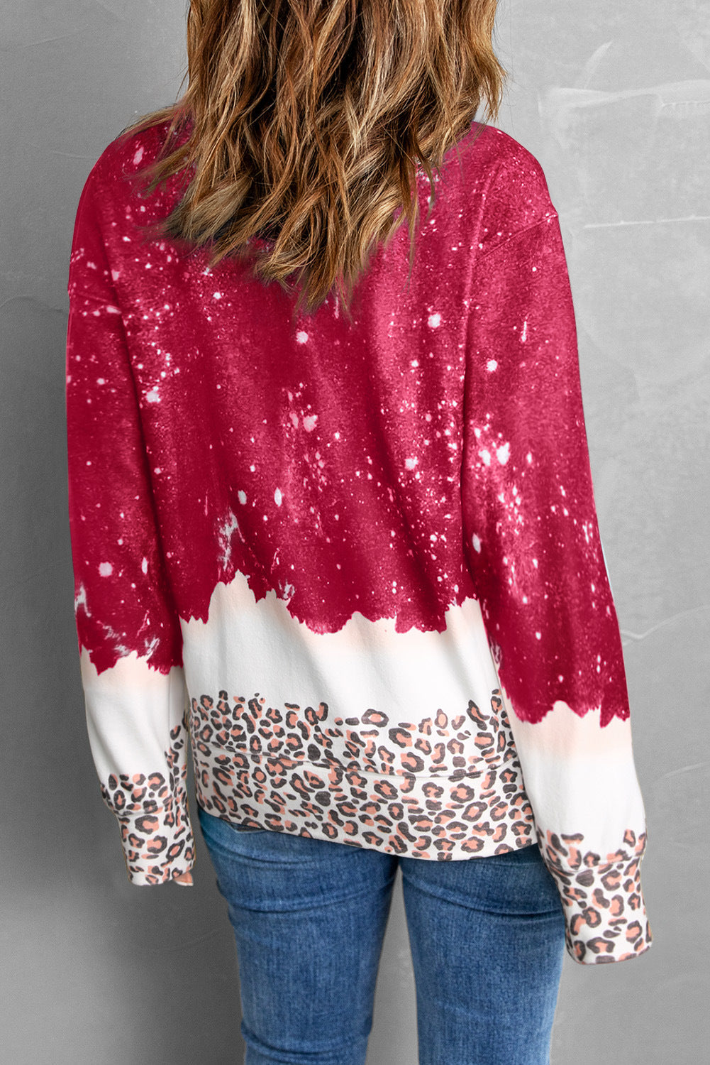 Donna con maglione rosso e bianco effetto spruzzato, motivo leopardato, jeans blu. Moda casual autunno, abbigliamento femminile trendy.