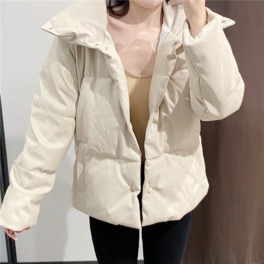 Giacca imbottita beige da donna, stile casual, con collo alto e bottoni, indossata sopra un top marrone chiaro. Moda invernale elegante.