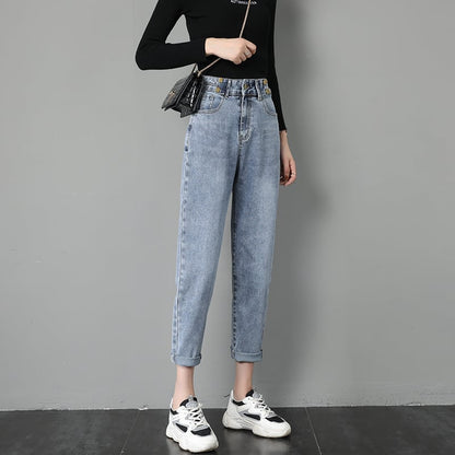 Donna in jeans a vita alta e maglia nera, con borsa a tracolla e sneakers bianche, posa contro un muro grigio. Moda casual femminile.