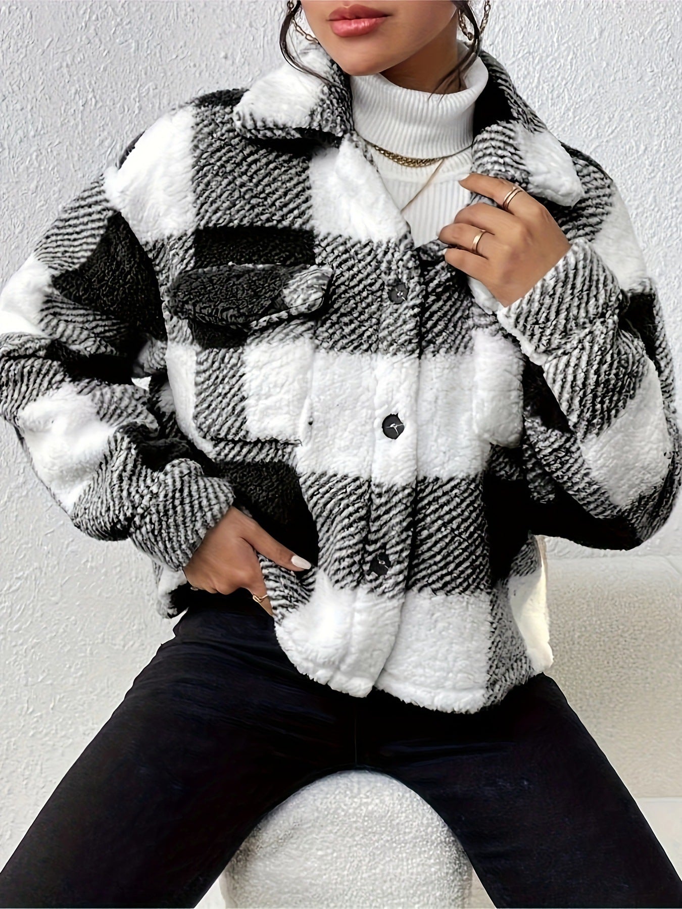 Donna con giacca a quadri bianca e nera, tessuto morbido, collo alto, indossa maglione bianco e jeans neri. Moda autunno inverno casual chic.