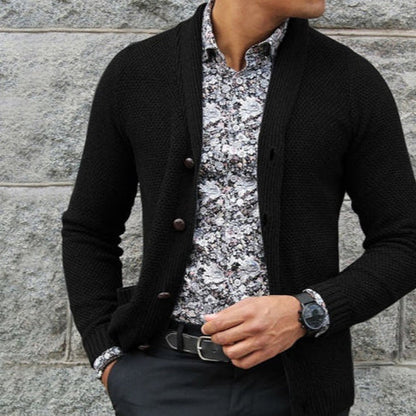 Uomo con cardigan nero, camicia a fiori bianca e nera, orologio da polso, pantaloni eleganti. Moda maschile autunnale, stile casual chic.