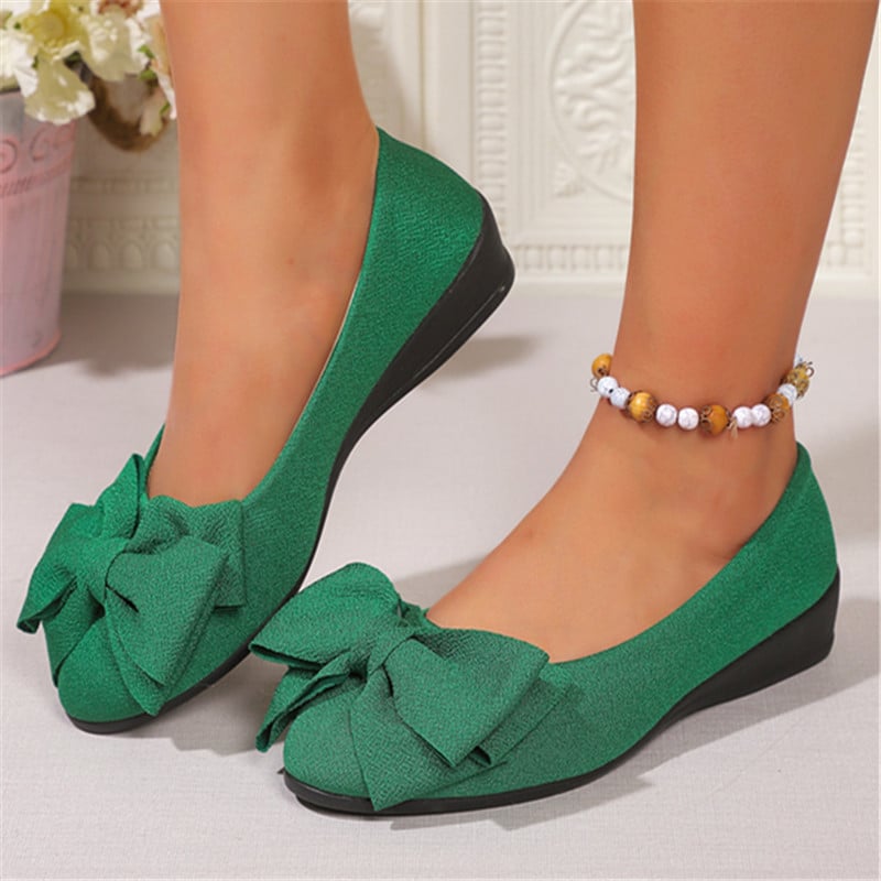 Scarpe ballerine verdi con fiocco, indossate su piedi femminili, abbinate a cavigliera con perline. Design elegante e moderno per moda donna.