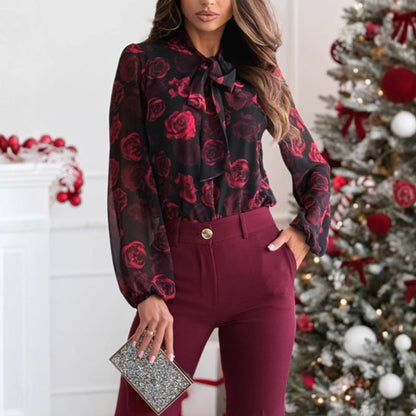 Donna in camicia floreale rossa e pantaloni bordeaux, tiene una pochette glitterata. Albero di Natale decorato sullo sfondo. Moda invernale elegante.