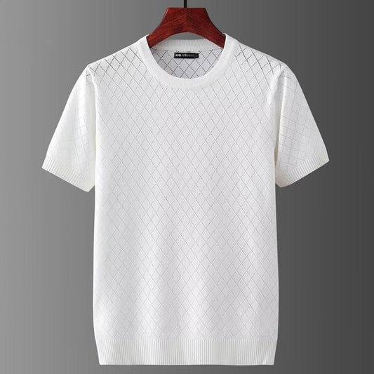 Maglietta bianca a maniche corte con motivo a rombi, appesa su gruccia di legno. Design elegante, ideale per moda estiva casual.