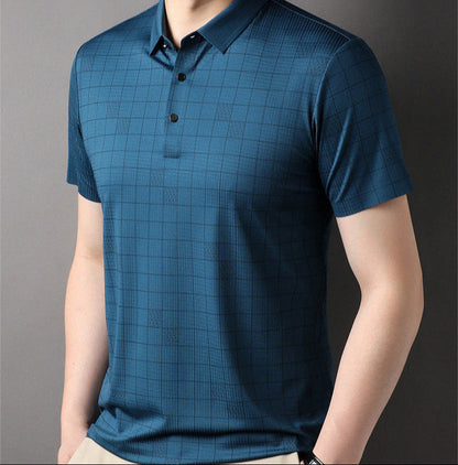 Maglietta polo blu a quadri, maniche corte, indossata da uomo su sfondo grigio. Stile casual elegante, moda maschile contemporanea.