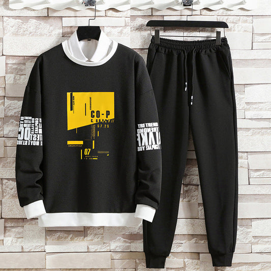 Completo sportivo uomo nero con grafica gialla e bianca, felpa e pantaloni, stile casual, moda streetwear, su sfondo di mattoni chiari.
