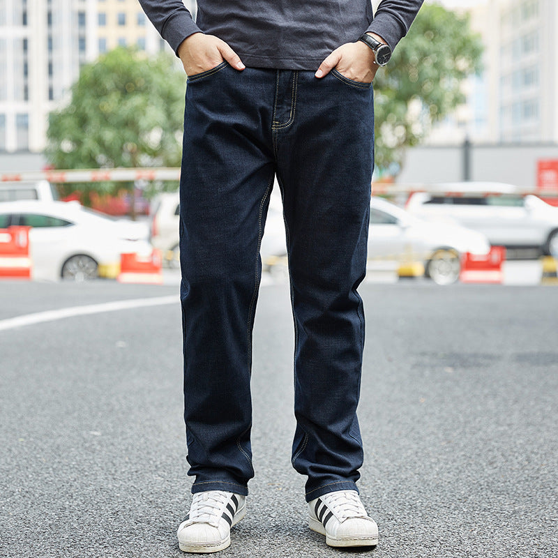 Uomo in jeans blu scuro e scarpe da ginnastica bianche su strada cittadina, sfondo urbano con auto parcheggiate. Moda casual maschile.