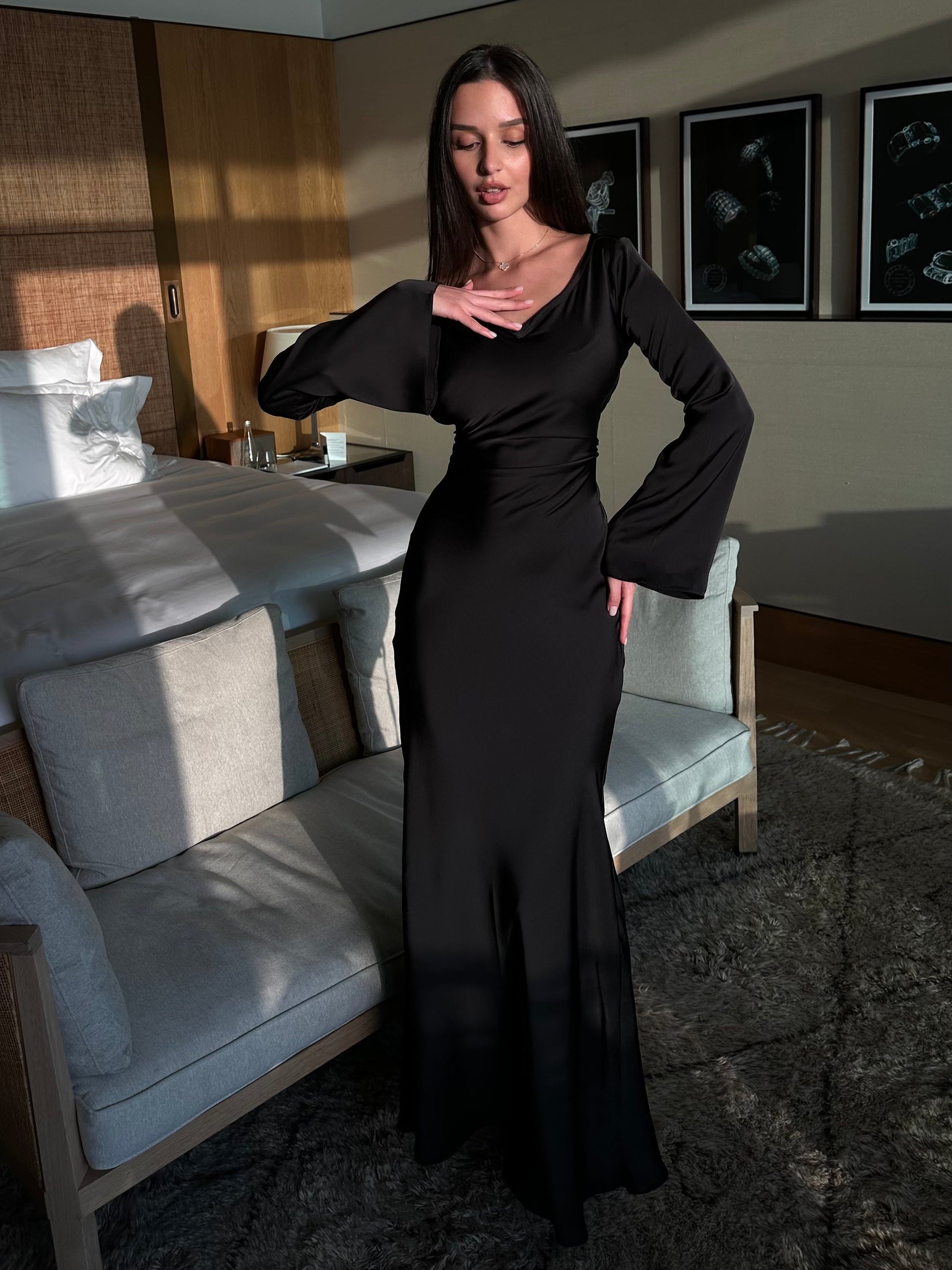 Donna in abito nero elegante in una camera da letto moderna, illuminata dalla luce naturale. Arredamento di lusso, atmosfera sofisticata.