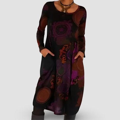 Abito lungo donna nero con motivi astratti viola e marroni, maniche lunghe, tasche laterali, collana dorata. Moda autunno, stile casual elegante.