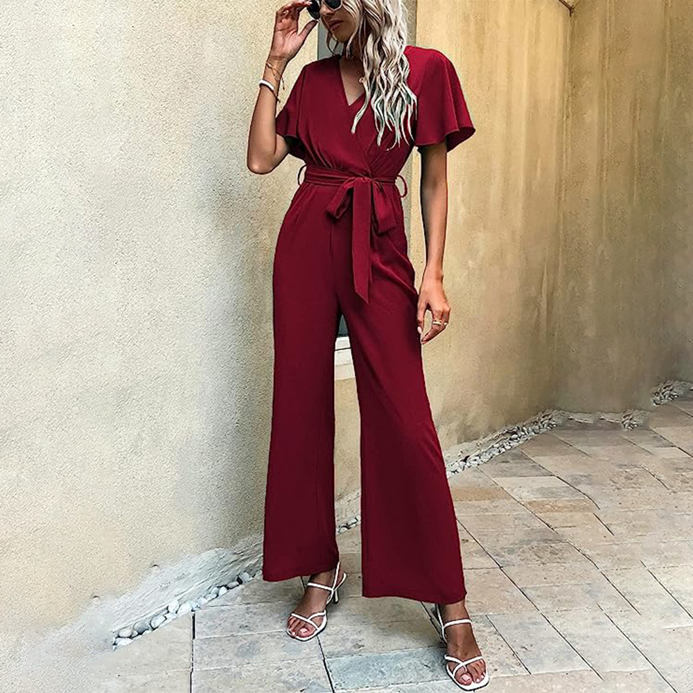 Donna con tuta rossa elegante, occhiali da sole, sandali bianchi, posa su pavimento in pietra. Moda estiva, abbigliamento femminile chic.